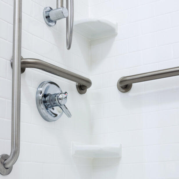 Stainless steel grab bars installed in a senior's bathroom beside the toilet and shower